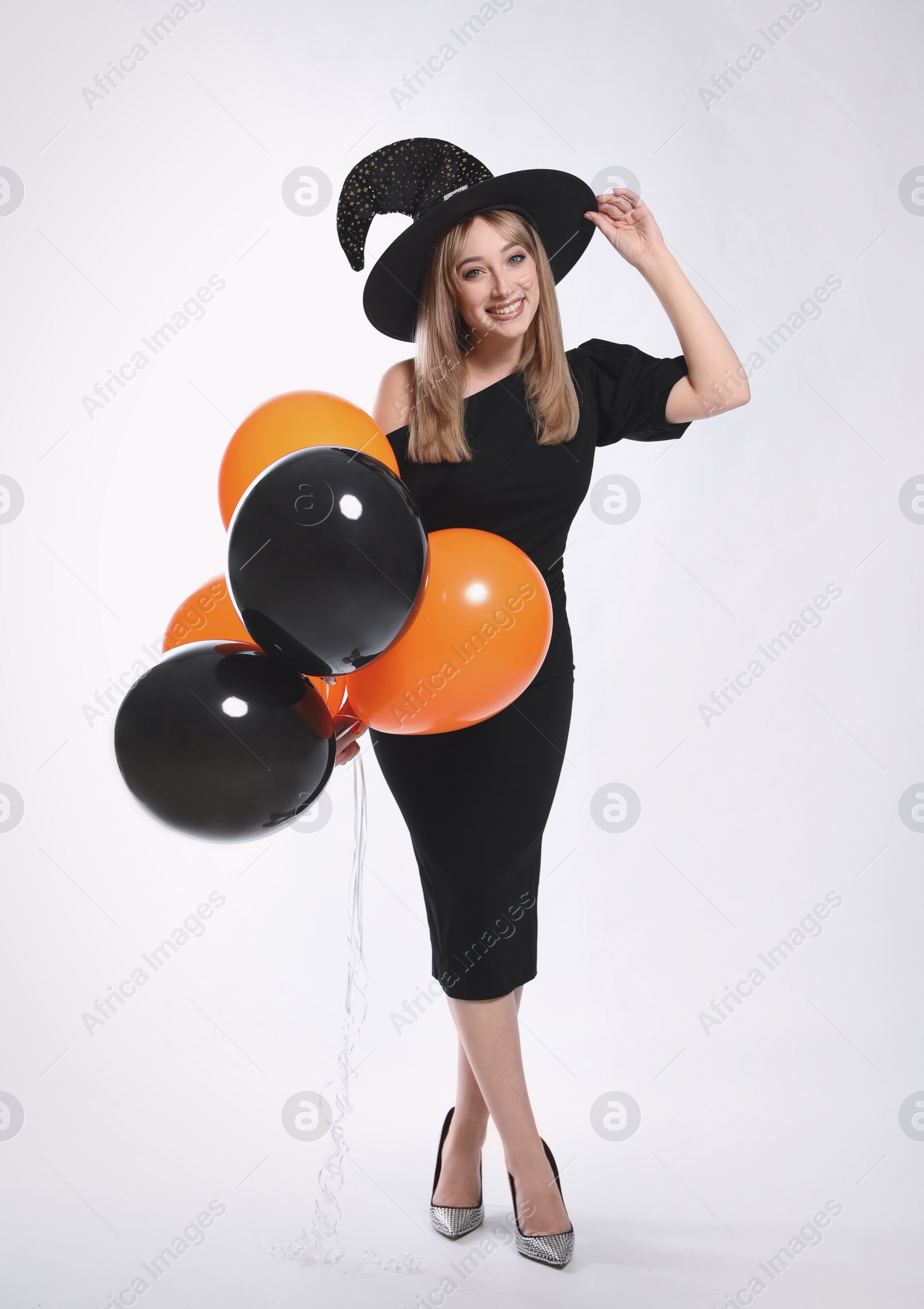 Photo of Beautiful woman in witch costume with balloons on white background. Halloween party