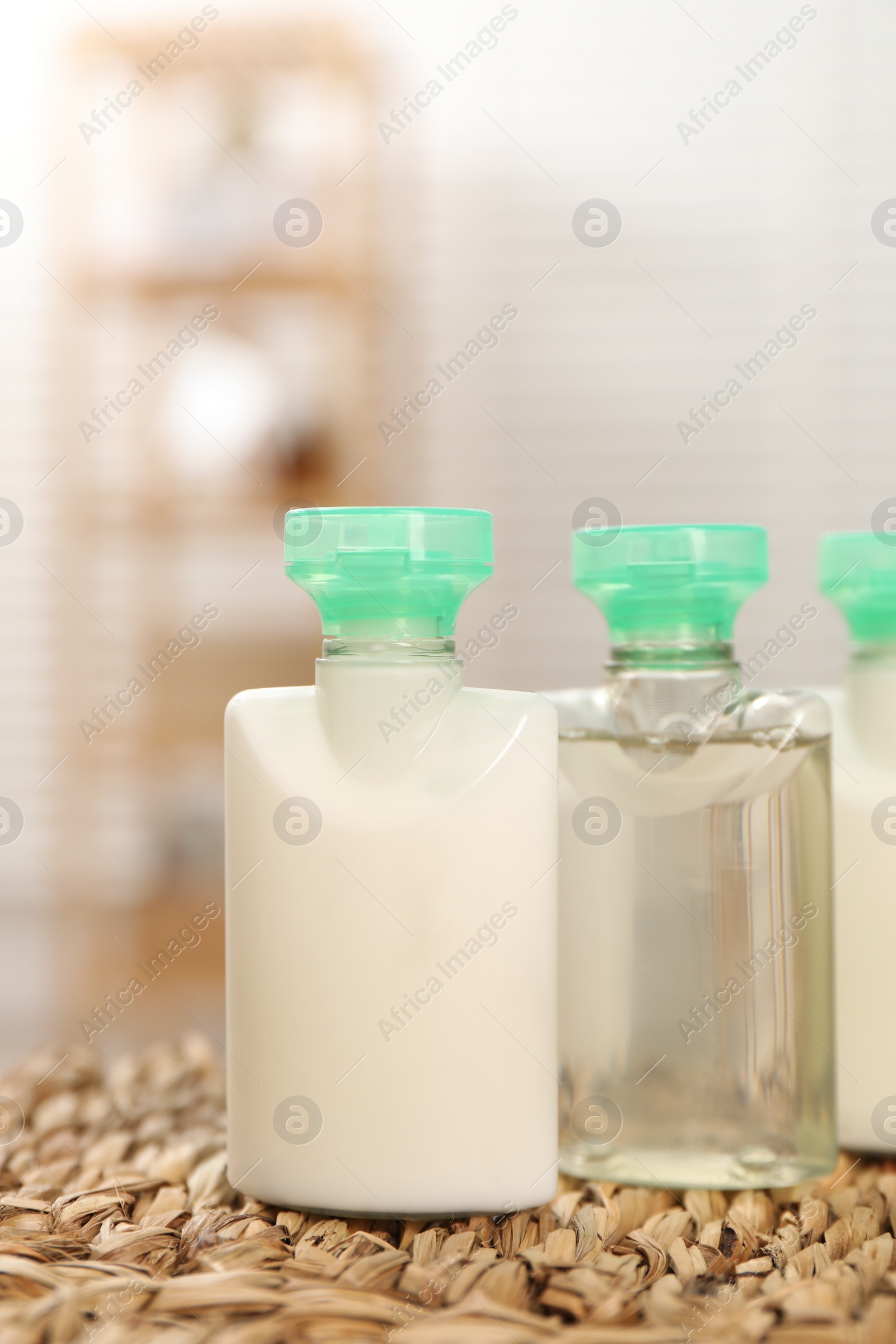 Photo of Mini bottles of cosmetic products on wicker mat against blurred background, closeup