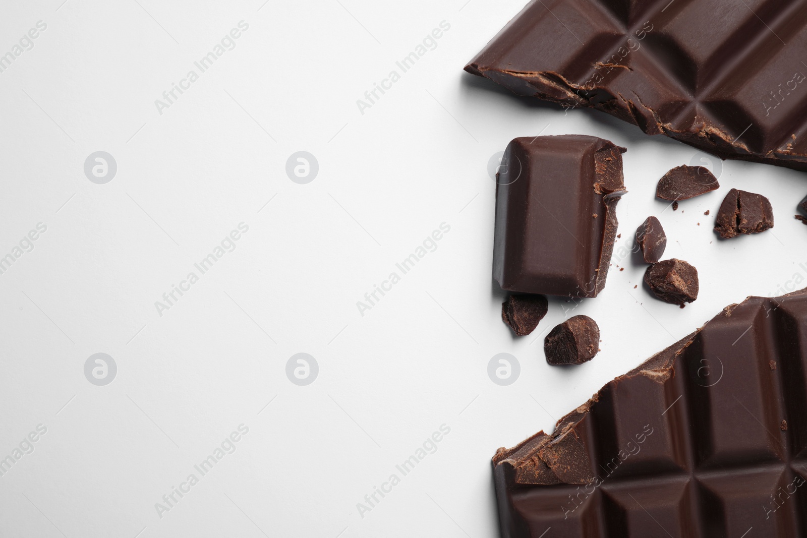 Photo of Pieces of delicious dark chocolate bar on white background, flat lay. Space for text