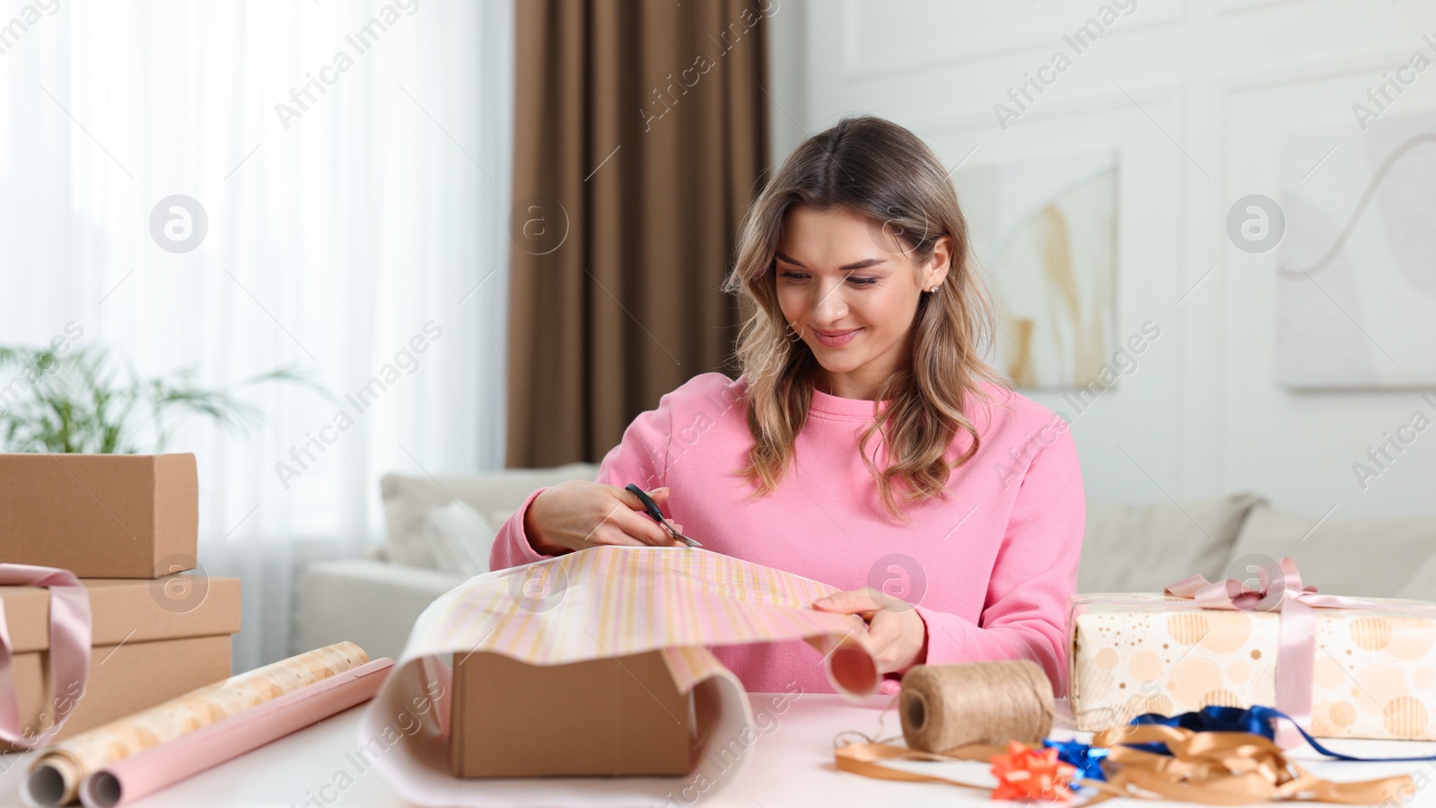 Photo of Beautiful young woman wrapping gift at table in living room