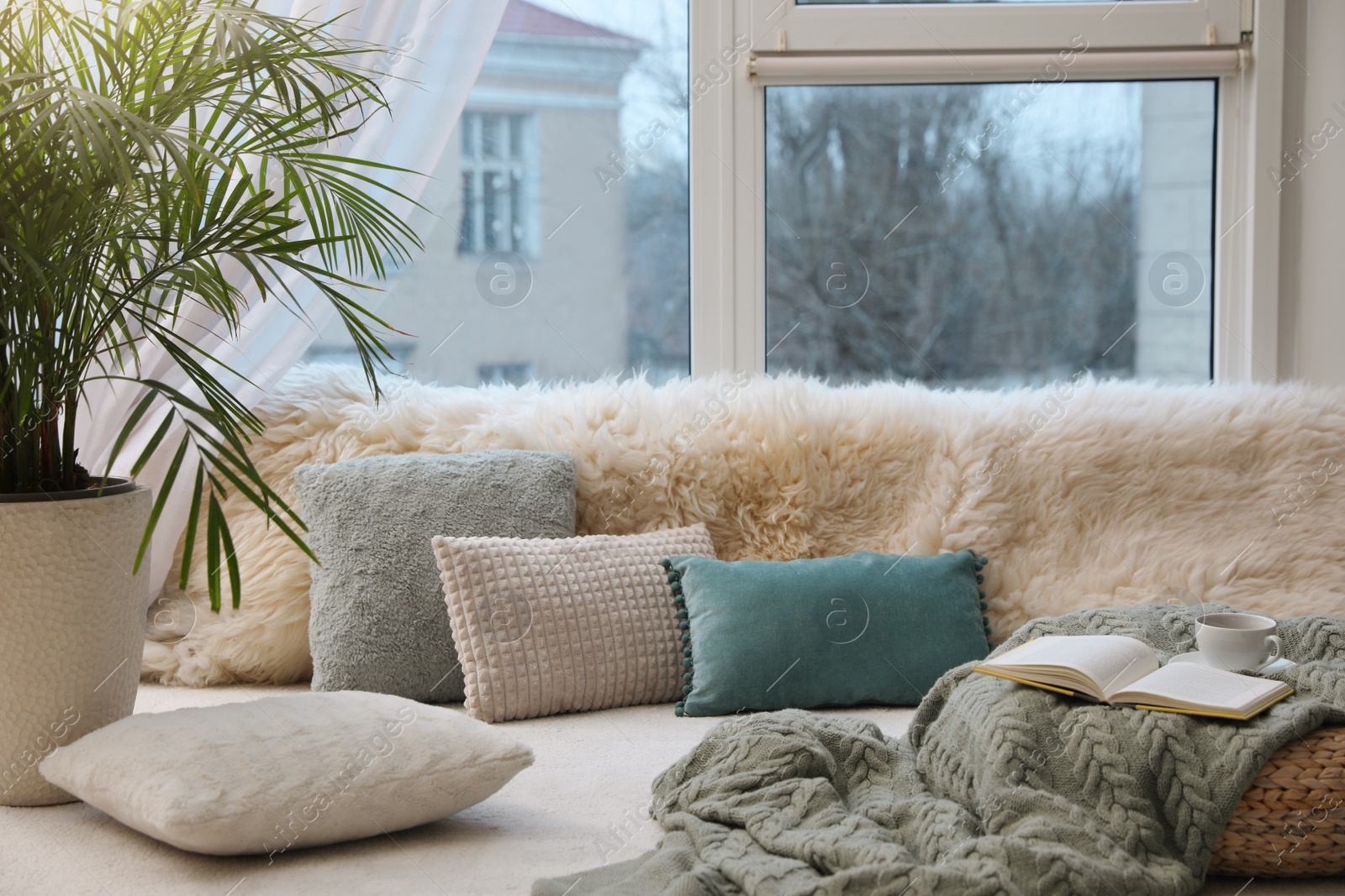 Photo of Comfortable lounge area with faux fur and pillows near window in room