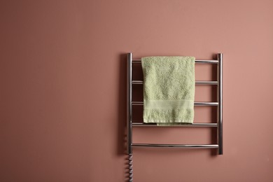 Photo of Modern heated towel rail with warm soft towel on pink wall. Space for text