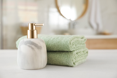 Photo of Clean towels and soap dispenser on white wooden table in bathroom