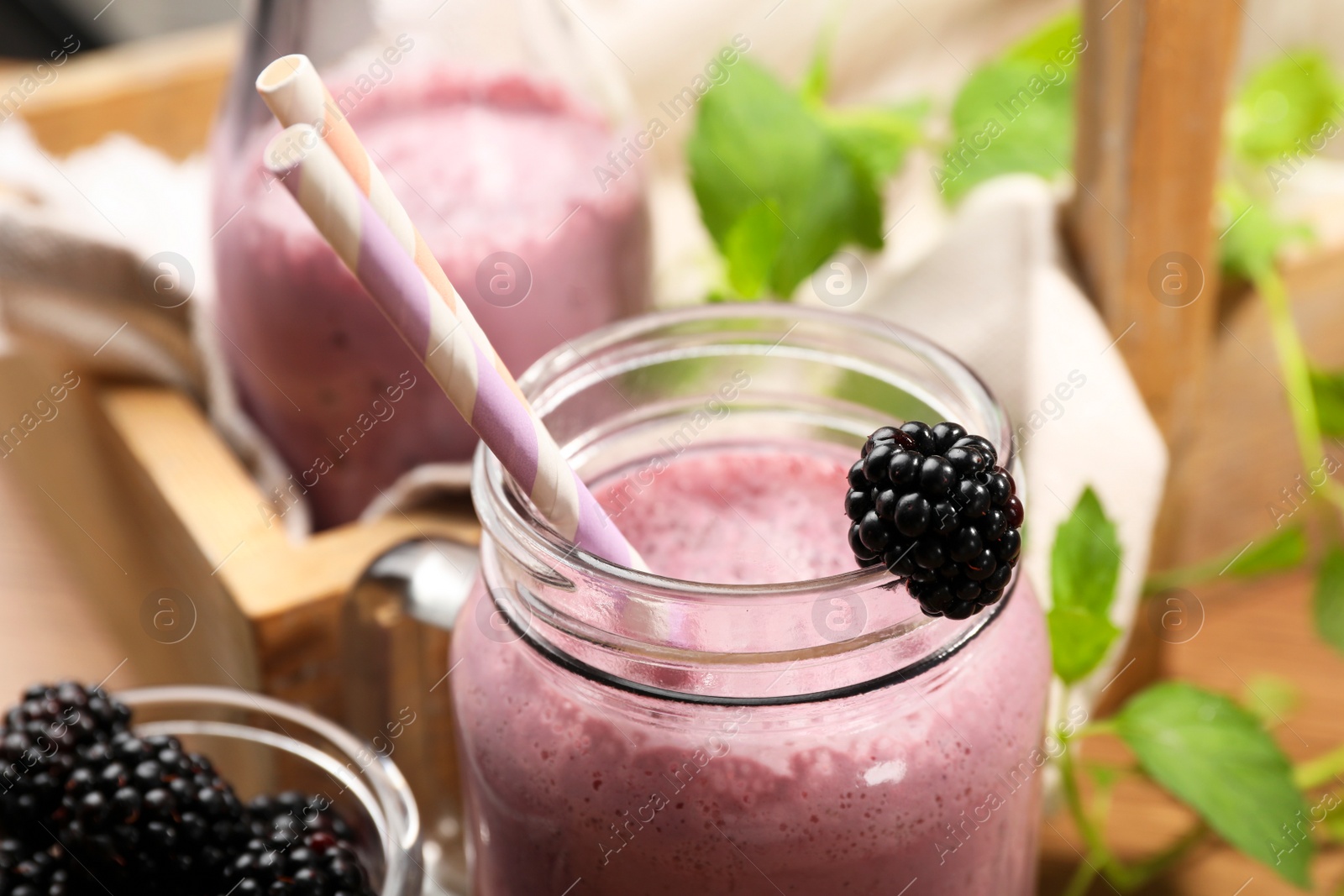 Photo of Different glassware of delicious blackberry smoothie and fresh berries on wooden background, closeup