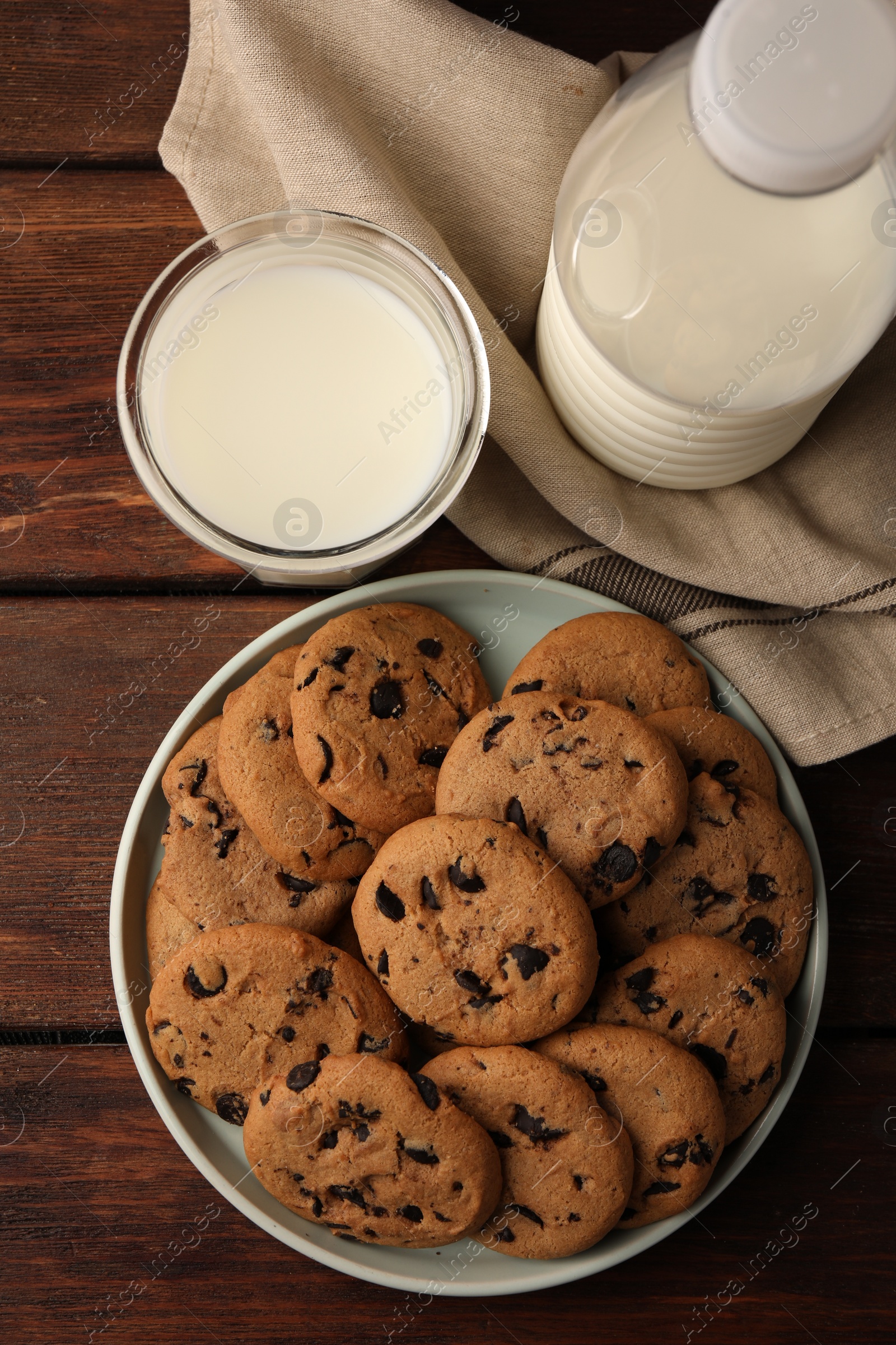 Photo of Delicious chocolate chip cookies and milk on wooden table, flat lay