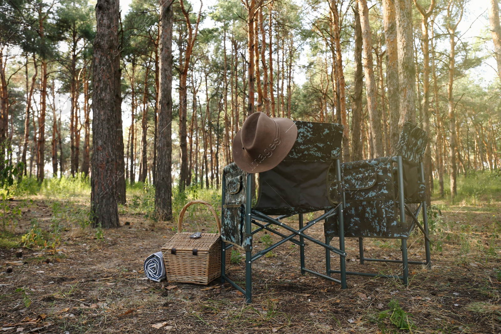 Photo of Camouflage chairs with hat and picnic basket in forest on sunny day