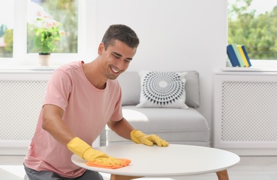 Photo of Man cleaning table with rag in living room