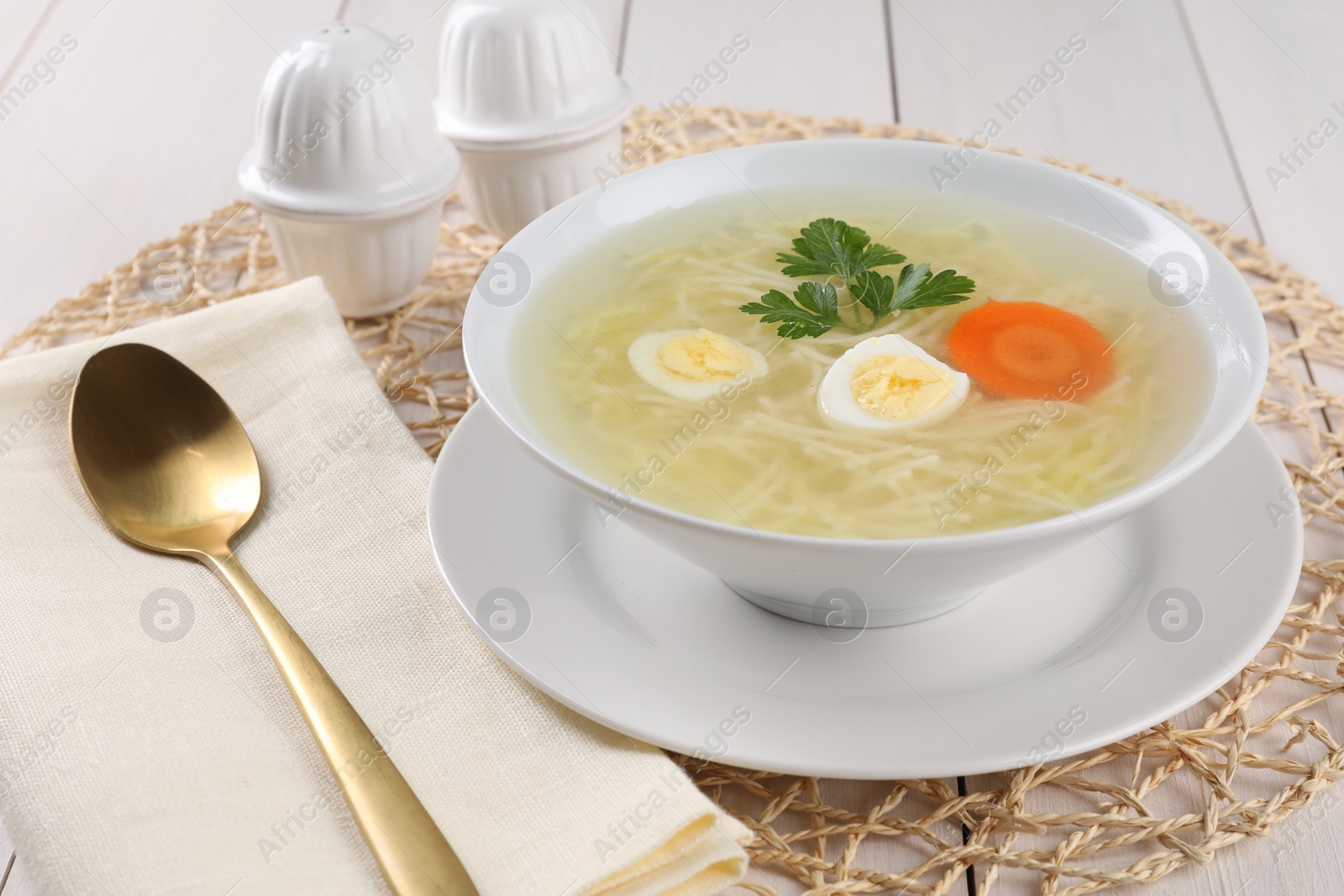 Photo of Tasty soup with noodles, egg, carrot and parsley in bowl served on white wooden table, closeup