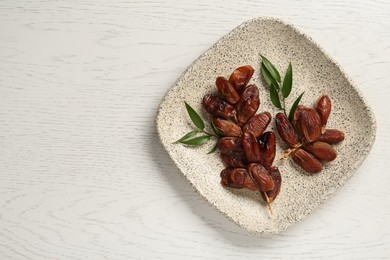 Photo of Plate with sweet dried dates and green leaves on white wooden table, top view. Space for text