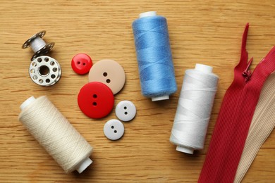 Flat lay composition with spools of threads and sewing tools on wooden table