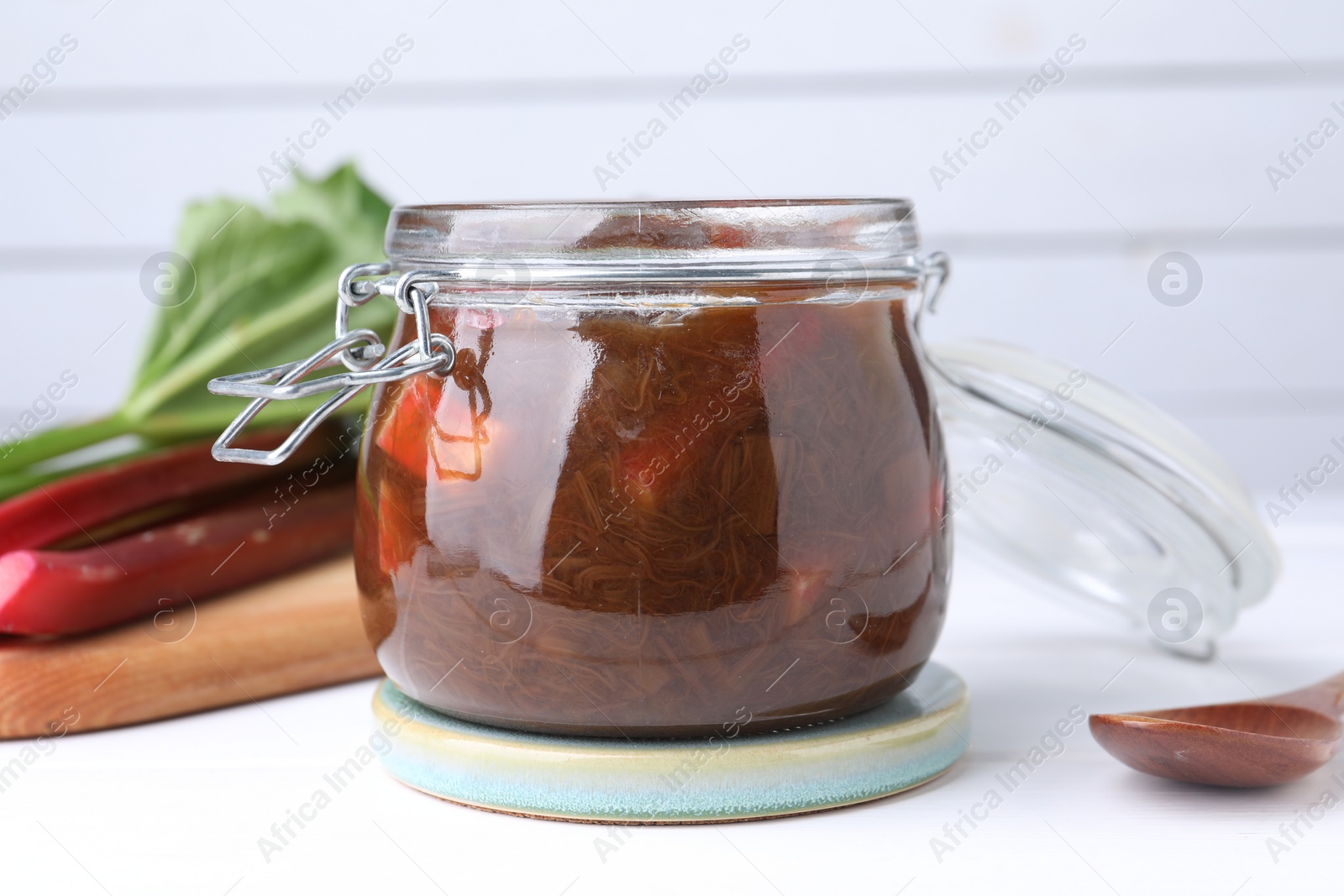 Photo of Jar of tasty rhubarb jam on white table, closeup