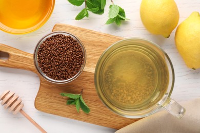 Photo of Cup of aromatic buckwheat tea, granules, lemons, mint and honey on white wooden table, flat lay
