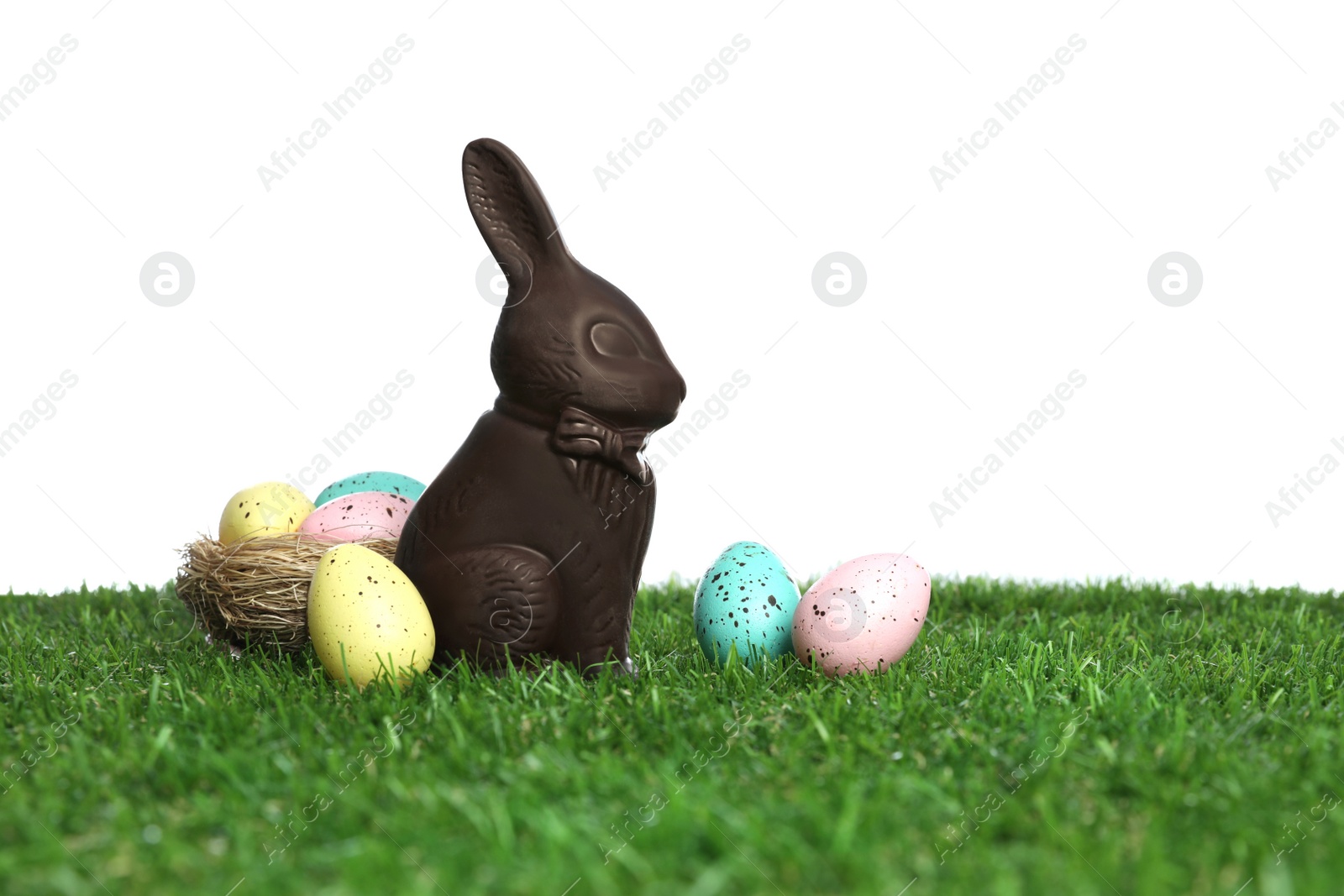 Photo of Chocolate bunny and eggs on green grass against white background, space for text. Easter celebration