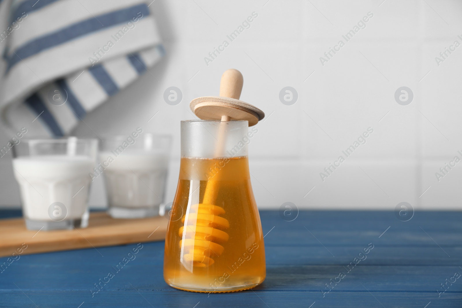 Photo of Jar with honey and glasses of milk on blue wooden table. Space for text