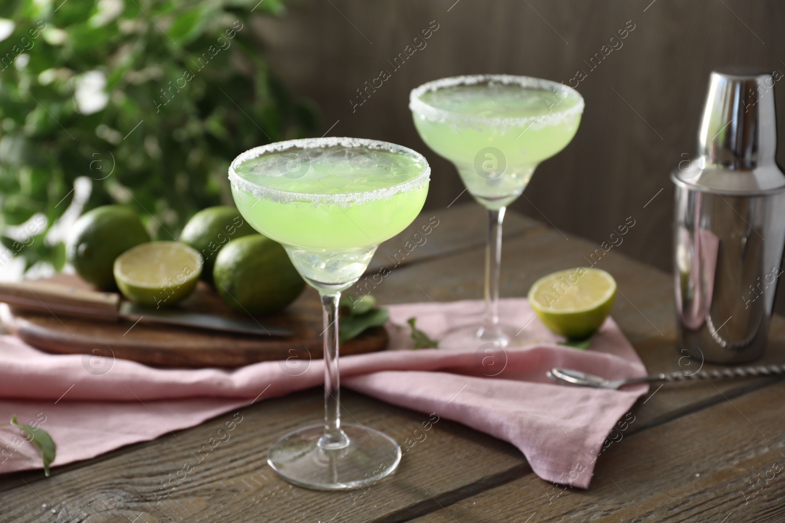 Photo of Delicious Margarita cocktail in glasses, lime and shaker on wooden table, closeup