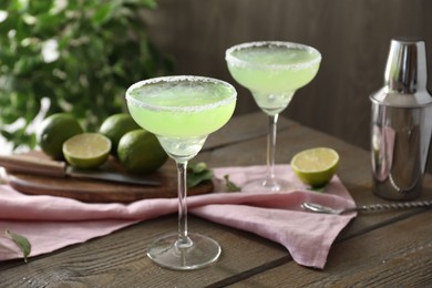 Photo of Delicious Margarita cocktail in glasses, lime and shaker on wooden table, closeup