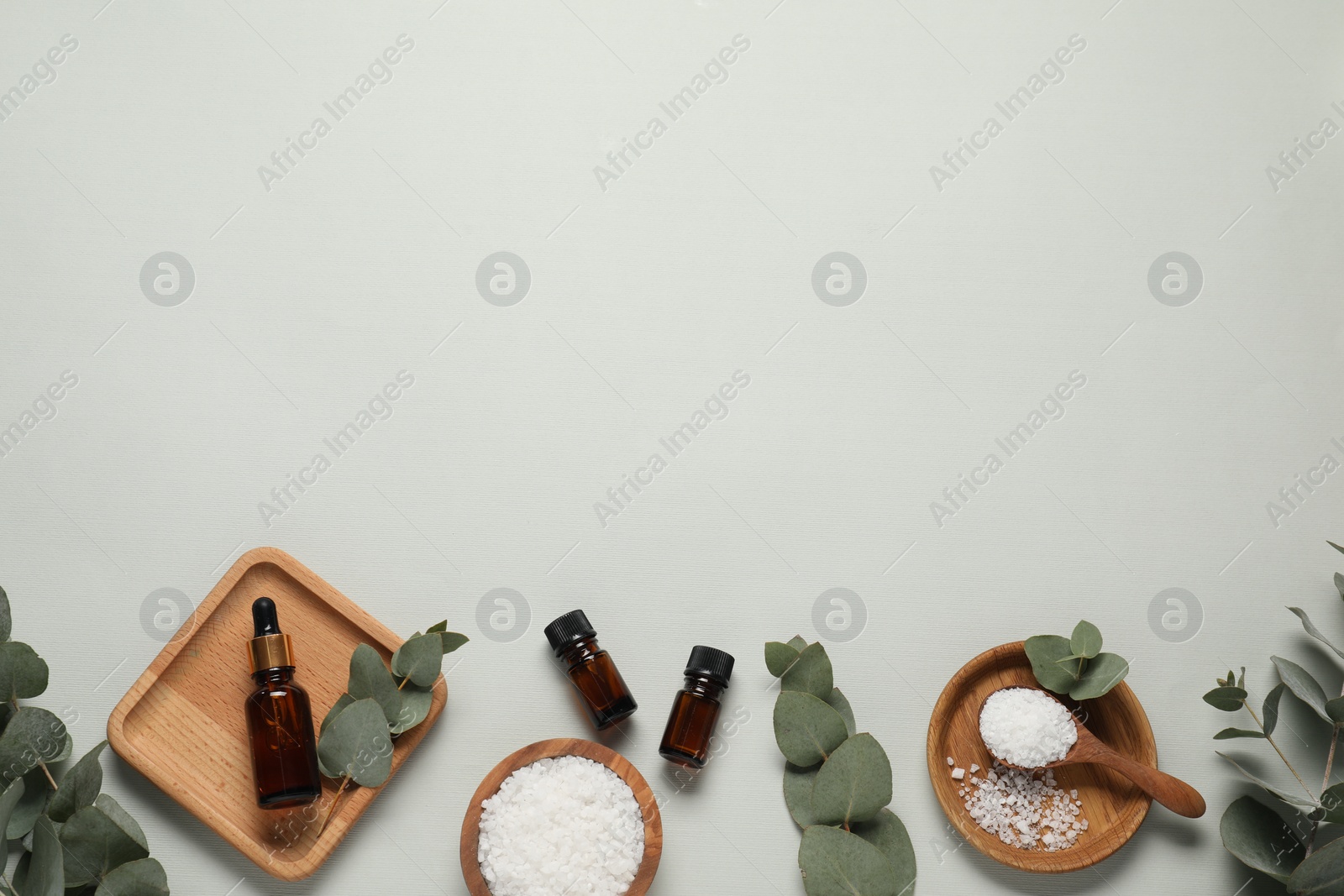 Photo of Aromatherapy products. Bottles of essential oil, sea salt and eucalyptus leaves on grey background, flat lay. Space for text