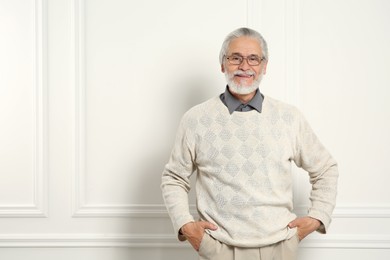 Portrait of handsome senior man in eyeglasses near white wall. Space for text