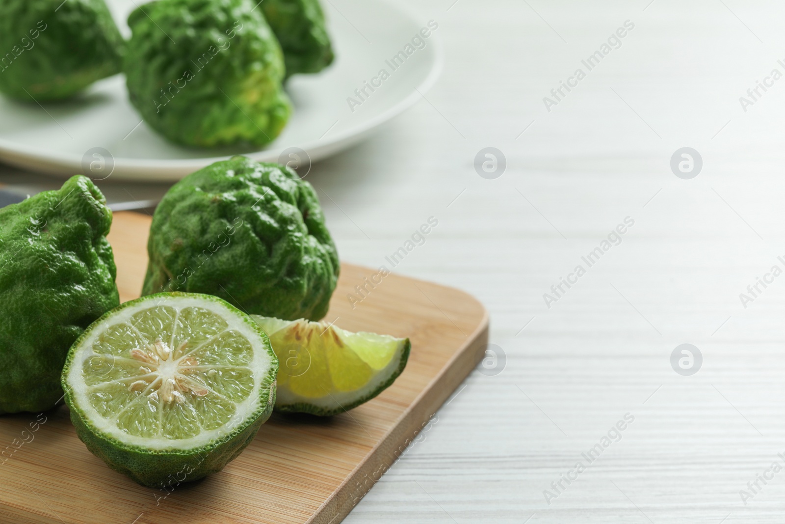 Photo of Whole and cut ripe bergamot fruits on white wooden table, space for text