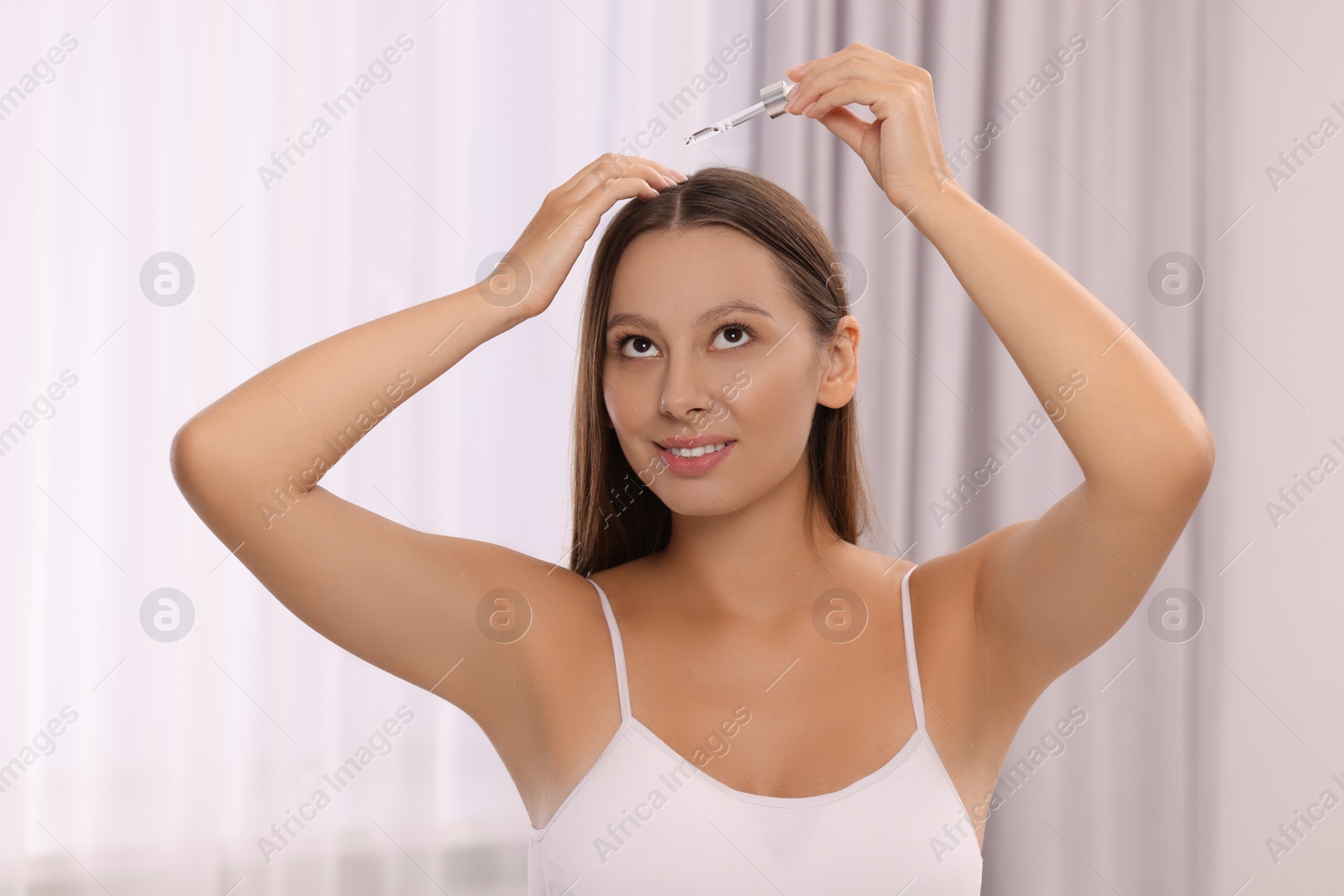 Photo of Beautiful woman applying serum onto hair indoors