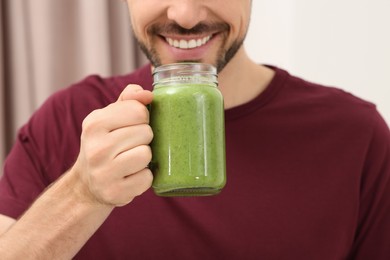 Photo of Happy man drinking delicious fresh smoothie indoors, closeup