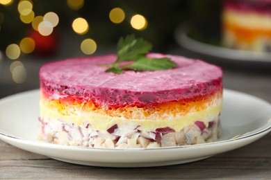 Photo of Herring under fur coat salad on white wooden table against blurred festive lights, closeup. Traditional Russian dish