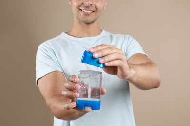 Photo of Young man holding deodorant on beige background, closeup. Mockup for design