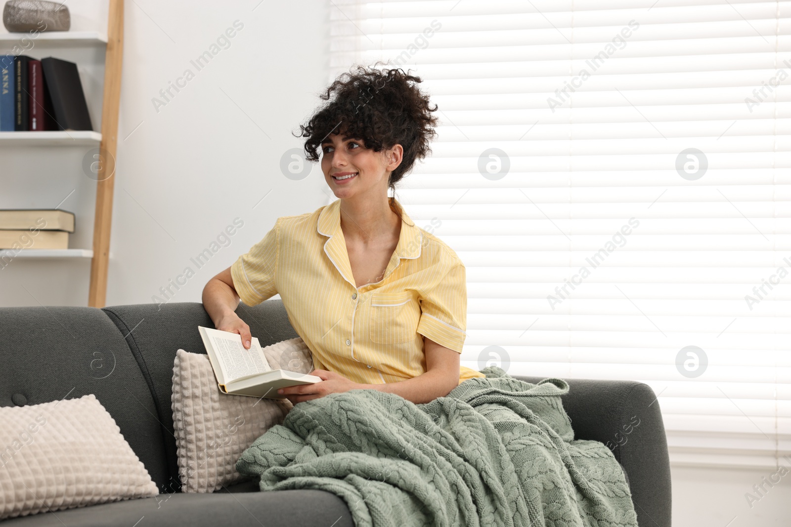 Photo of Beautiful young woman in stylish pyjama with book on sofa at home