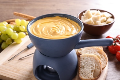 Board with pot of cheese fondue and bread on table