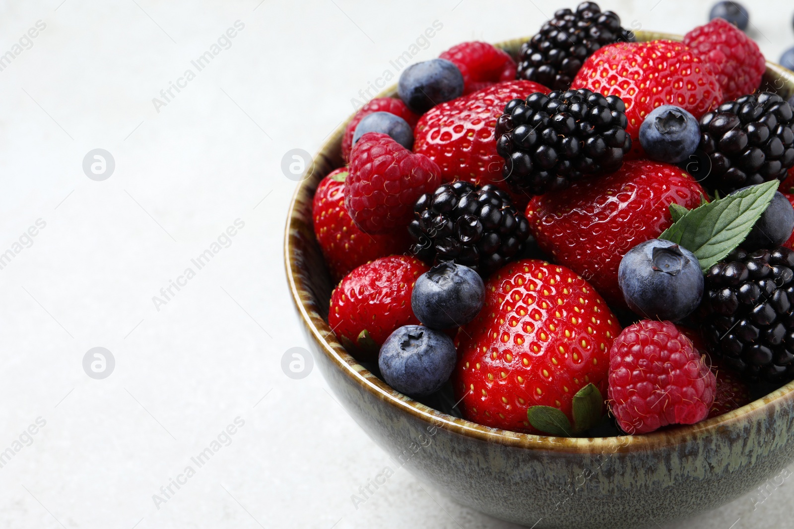 Photo of Different fresh ripe berries in bowl on light grey table, closeup. Space for text