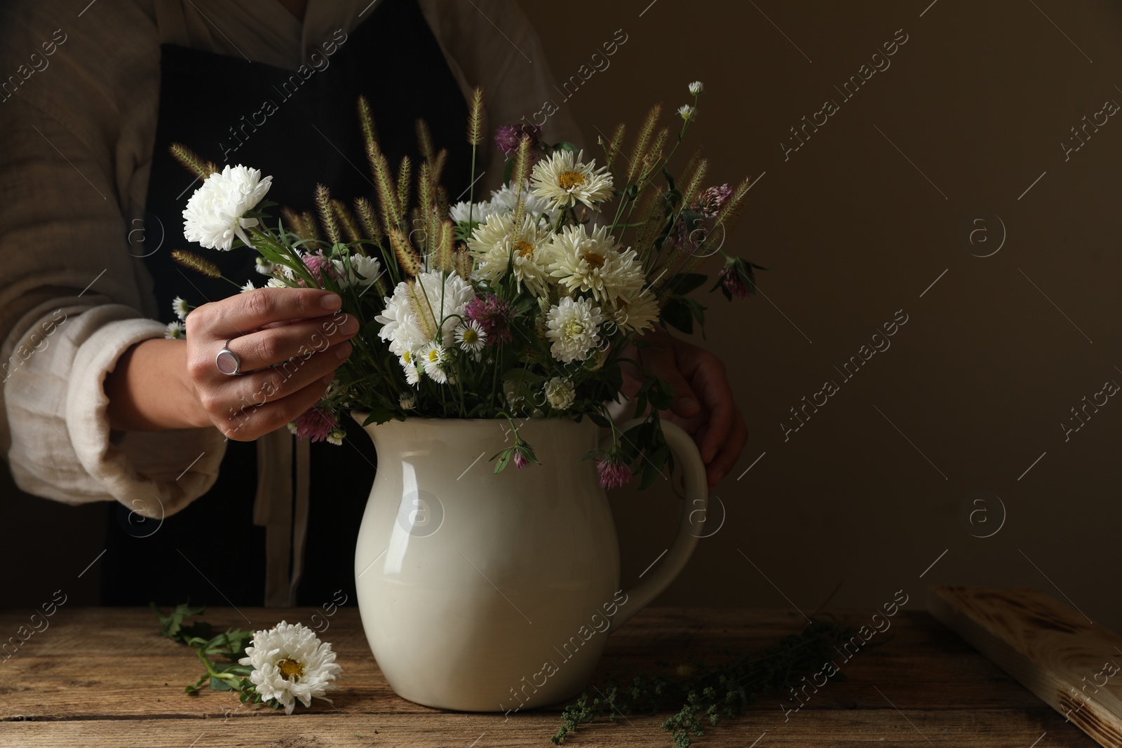 Photo of Woman creating beautiful flower arrangement at wooden table, closeup. Space for text