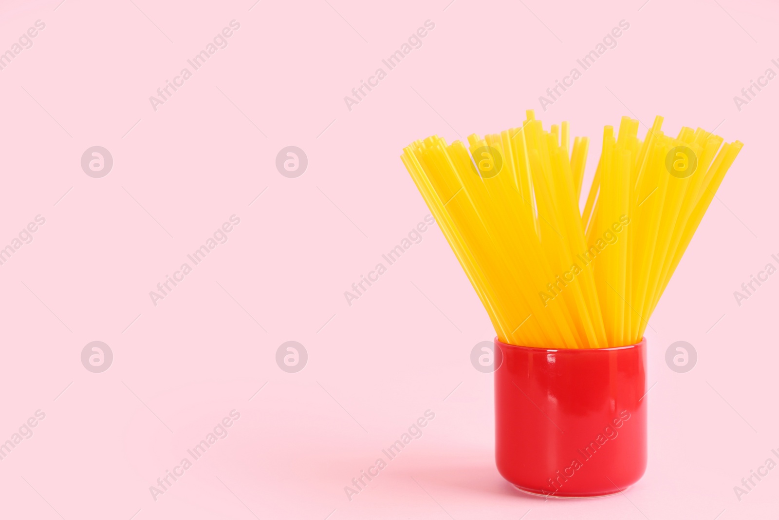 Photo of Yellow plastic drinking straws in holder on pink background, space for text