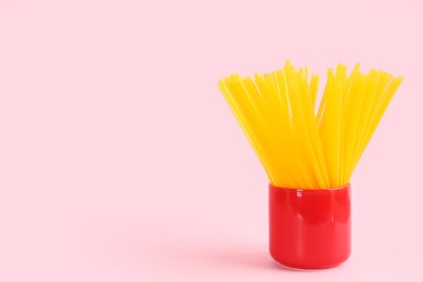 Photo of Yellow plastic drinking straws in holder on pink background, space for text
