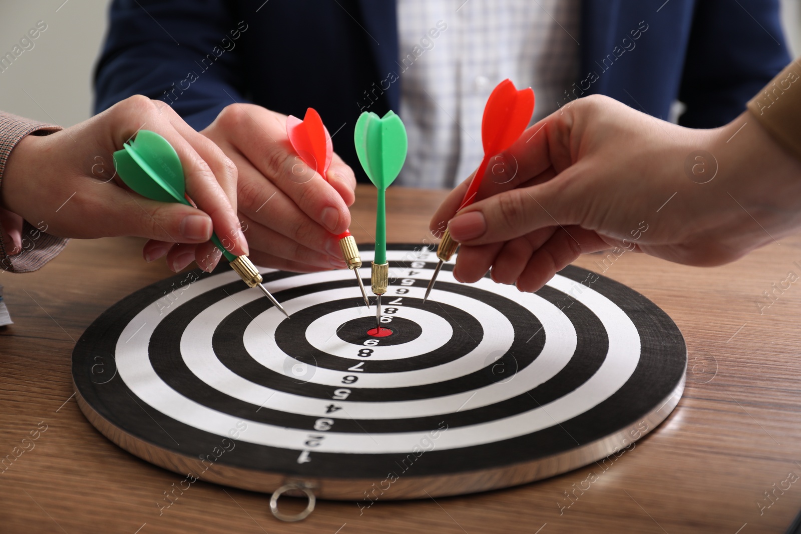 Photo of Business targeting concept. People with darts aiming at dartboard at wooden table, closeup