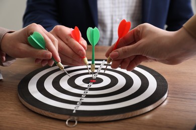 Business targeting concept. People with darts aiming at dartboard at wooden table, closeup