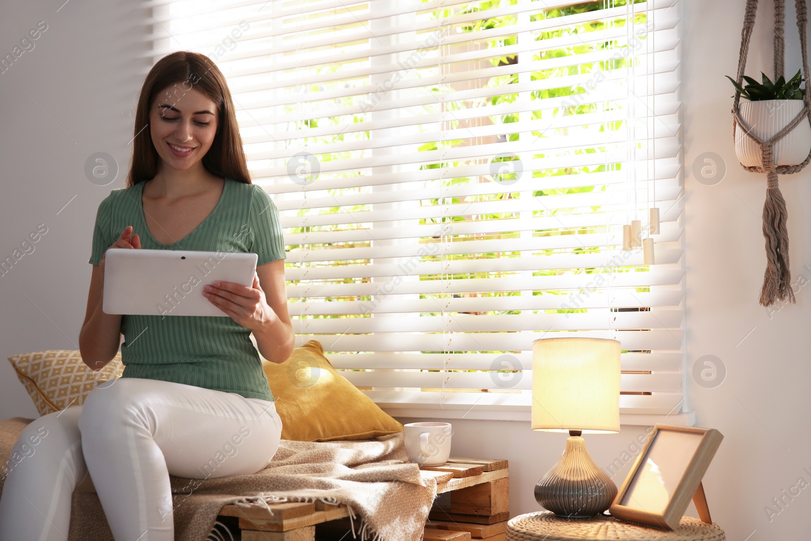 Photo of Beautiful young woman using tablet near window at home