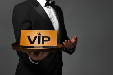 Man holding tray with VIP sign on grey background, closeup. Space for text