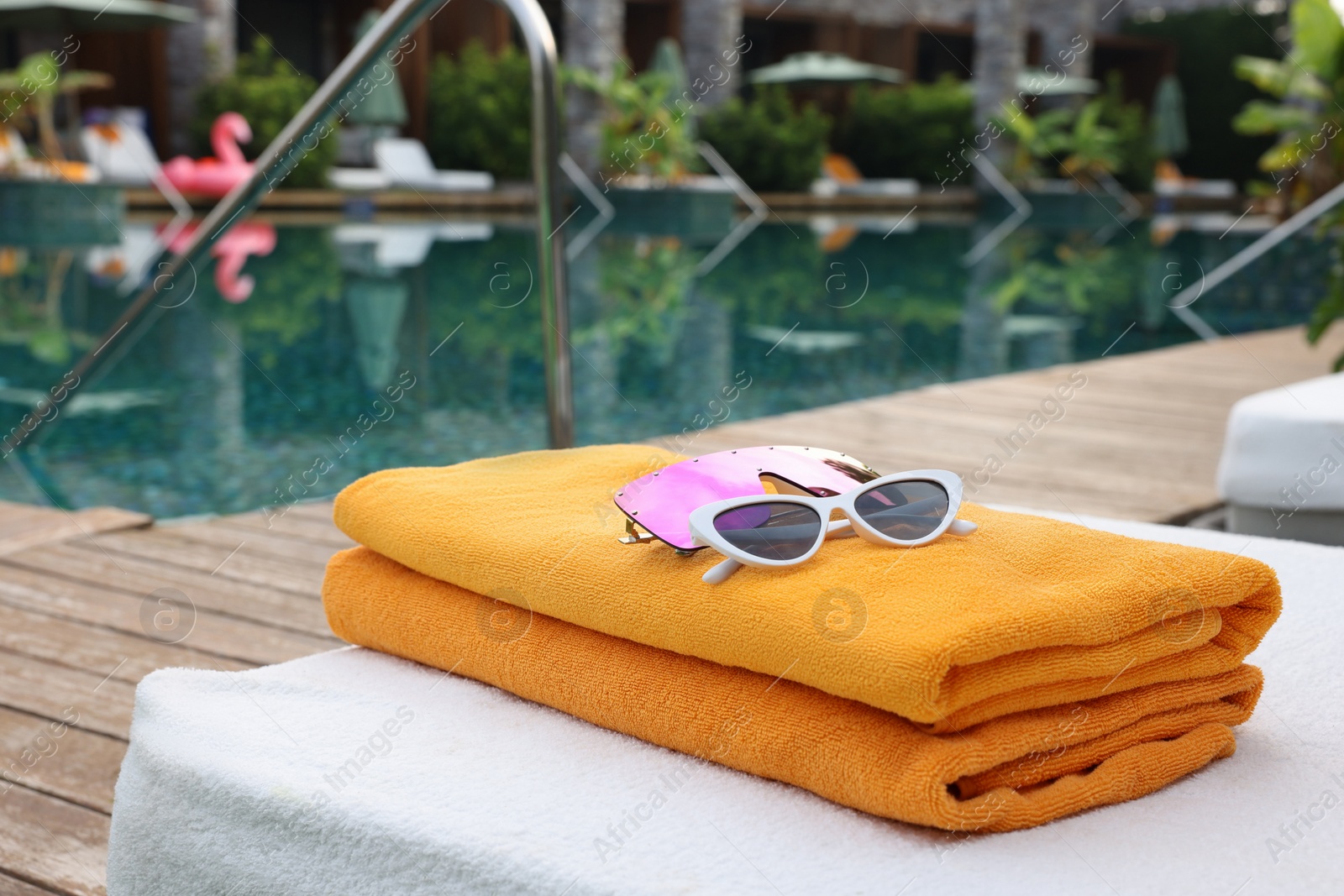 Photo of Beach towels and sunglasses on sun lounger near outdoor swimming pool. Luxury resort