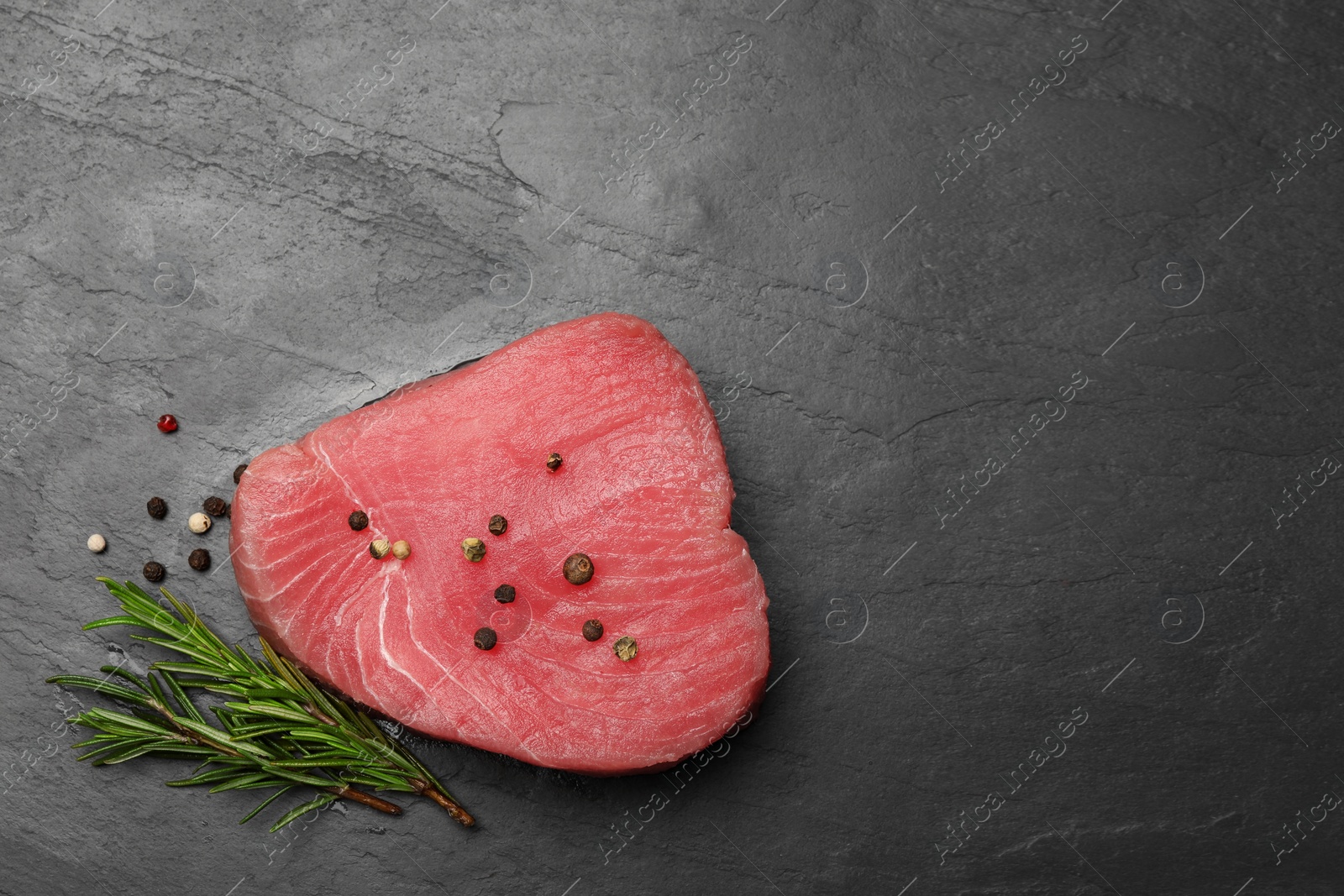 Photo of Raw tuna fillet with peppercorns and rosemary on black table, flat lay. Space for text