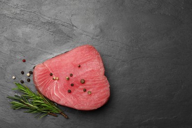 Raw tuna fillet with peppercorns and rosemary on black table, flat lay. Space for text