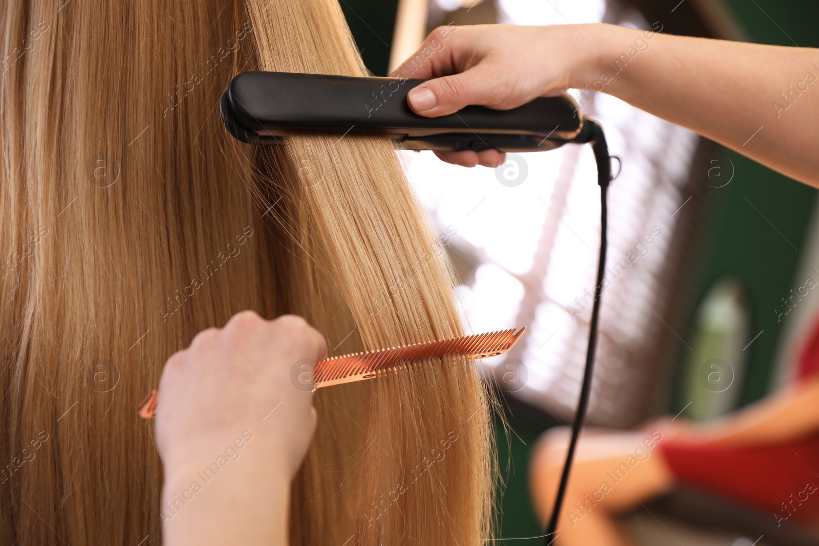 Photo of Stylist straightening woman's hair with flat iron in salon, closeup