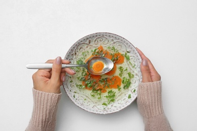 Photo of Woman with bowl of soup at white table, top view. Flu treatment