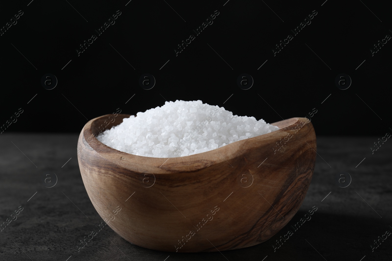 Photo of Natural salt in wooden bowl on dark grey table, closeup