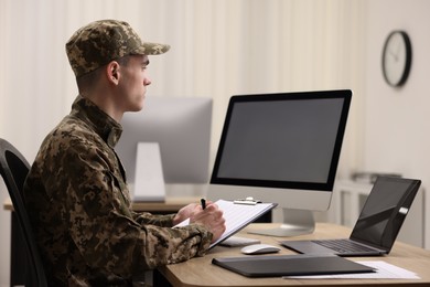 Photo of Military service. Soldier with clipboard working at table in office