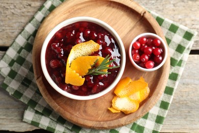 Photo of Cranberry sauce in bowl, fresh berries, rosemary and orange peels on wooden table, top view