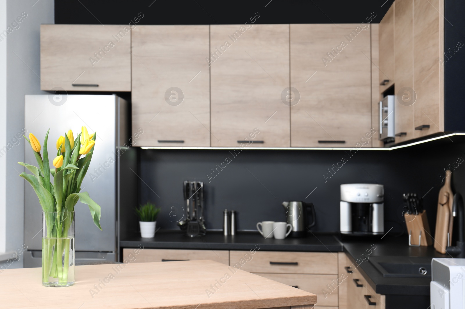 Photo of Vase with tulips on table in cozy modern kitchen interior, selective focus