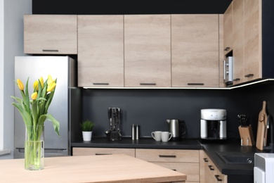 Vase with tulips on table in cozy modern kitchen interior, selective focus