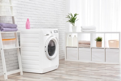 Photo of Modern washing machine near brick wall in laundry room interior