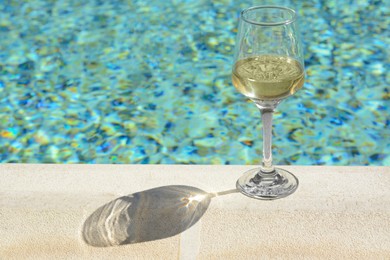 Glass of tasty wine on swimming pool edge, space for text