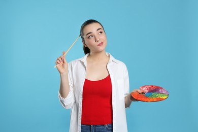 Photo of Woman with painting tools on light blue background. Young artist